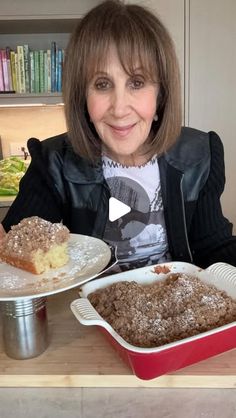 a woman sitting at a table with two plates of food and a pan of cake