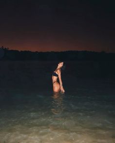 a woman standing in the ocean at night with her head above the water's surface