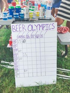 a beer olympics sign sitting on top of a grass covered field next to a picnic table