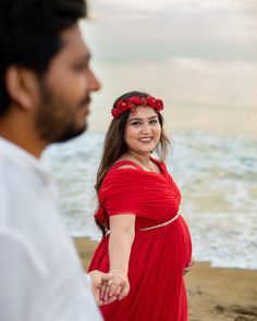 a pregnant woman in a red dress holding hands with a man standing next to her