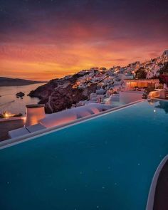 an outdoor swimming pool at night with the sun setting over the water and buildings in the background