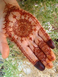 a person's hand with henna on it and some plants in the background