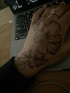 a person's hand with a flower tattoo on their left wrist, next to a laptop