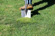 a person standing on top of a green field next to a metal shovel and fork