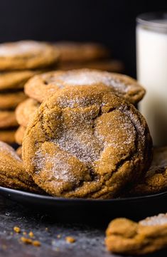 a plate full of cookies next to a glass of milk on a table with some powdered sugar