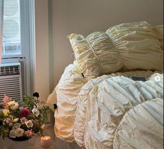 a white bed sitting next to a window filled with flowers and blankets on top of it