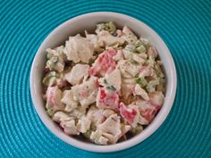 a white bowl filled with chicken salad on top of a blue place mat next to a fork