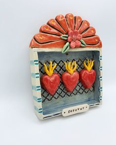 three red hearts with yellow crowns in a decorative box