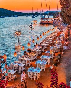 an outdoor dining area with tables and chairs on the water at sunset or dawn,