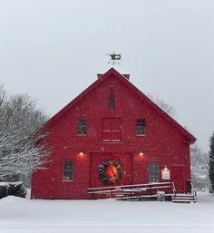 a red barn with a wreath on the door and lights in the windows is surrounded by snow