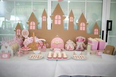 a table topped with lots of pink and white desserts next to a castle shaped wall