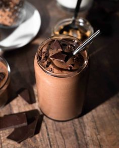 two glasses filled with chocolate and ice cream on top of a wooden table next to spoons