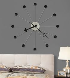 a large clock mounted to the side of a gray wall next to a night stand