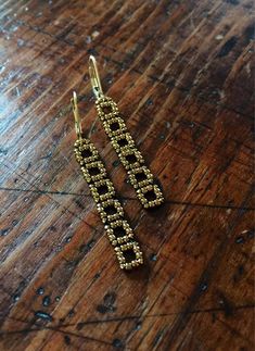 two pairs of gold earrings sitting on top of a wooden table next to each other