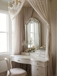 a white dressing table with a mirror, stool and chandelier