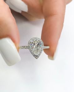 a woman's hand holding a ring with a pear shaped diamond on top of it