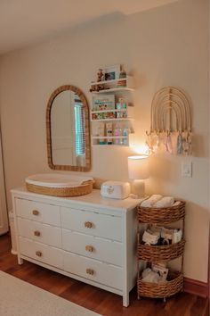 a white dresser sitting in a bedroom next to a wall mounted mirror and shelf filled with baby items