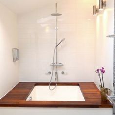 a bathroom with a sink, shower head and wooden counter top in it's corner