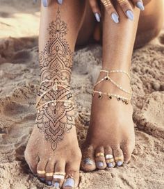 a woman's feet with tattoos and jewelry on the sand in front of her