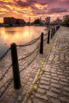 the sun is setting over a body of water with chain link fence in front of it