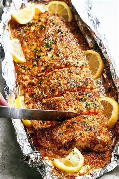 someone cutting up some food on top of tin foil with lemons and parsley