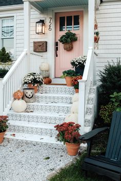 front porch decorated for halloween with pumpkins and flowers on the steps to the door