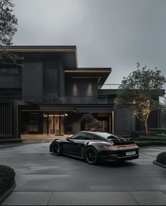 a black sports car is parked in front of a large house with trees and bushes