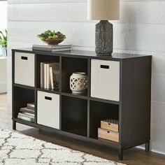 a black and white bookcase with four bins next to a lamp on a rug