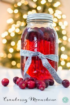 a jar filled with cranberry moonhine sitting on top of a table next to a christmas tree