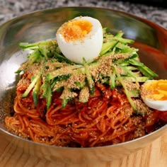 a bowl filled with noodles and vegetables topped with an egg on the top, sitting on a wooden table