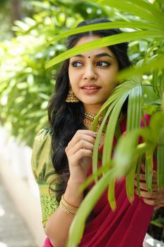 a woman in a red sari is posing for the camera with green plants behind her