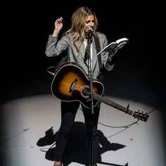 a woman singing into a microphone and holding a guitar in front of her face while standing on a stage