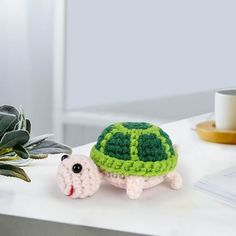 a crocheted turtle sitting on top of a table next to a potted plant