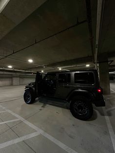 a black jeep parked in an empty parking garage with no one around the vehicle and it's door open