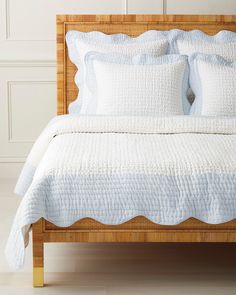 a bed with white linens and pillows on top of it, in front of a wall