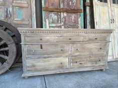 an old wooden dresser sitting on top of a sidewalk next to some doors and a wagon wheel