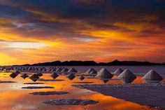 the sun is setting over an array of sand mounds in the water at low tide