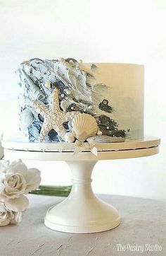 there is a white cake with blue icing and shells on the top, along with flowers