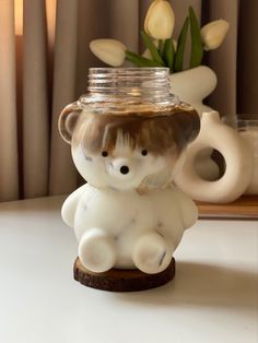 there is a small glass bear with a jar on it's head and flowers in the background