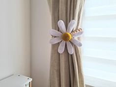 a white and yellow flower hanging on the side of a curtain in front of a window