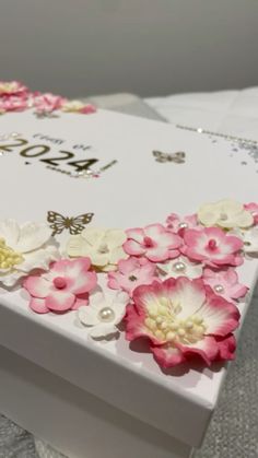 a white box with pink and white flowers on it's side, sitting on a table