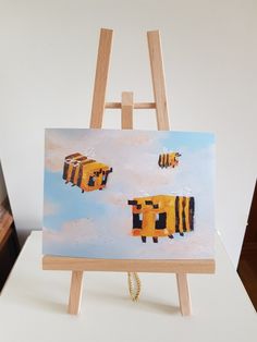 an easel with a painting on it and two bees flying in the sky