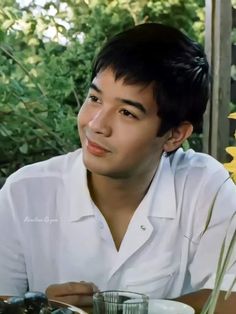 a man sitting at a table with food in front of him and flowers behind him