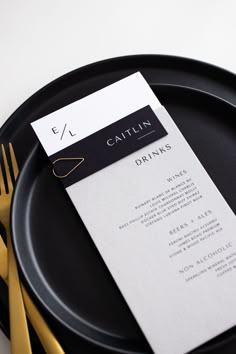 a black plate with a white menu card on it and gold utensils next to it