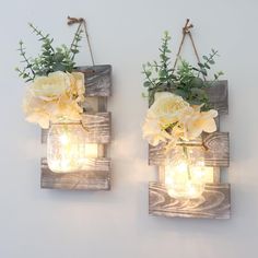 two mason jars with flowers are hanging on the wall next to each other, one is filled with light bulbs