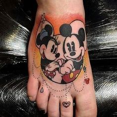 a mickey mouse tattoo on the foot of a person's hand with hearts around it