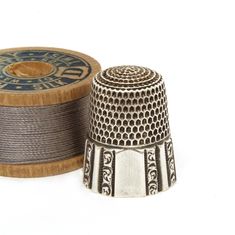 a silver thimble next to a spool of thread on a white background