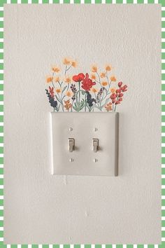 an electrical outlet with flowers painted on the wall and in between two white switchesticks