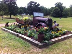 an old truck sitting in the middle of a flower bed with flowers growing out of it