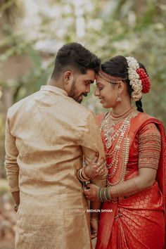 a man and woman standing next to each other in front of some trees with their hands together